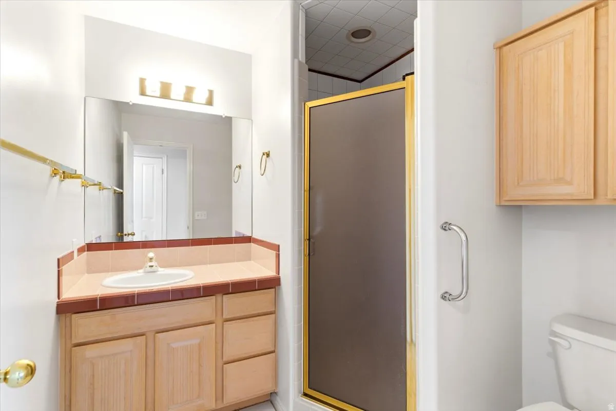 Bathroom vanity featuring a single basin, tiled countertop, and wood-finish cabinetry