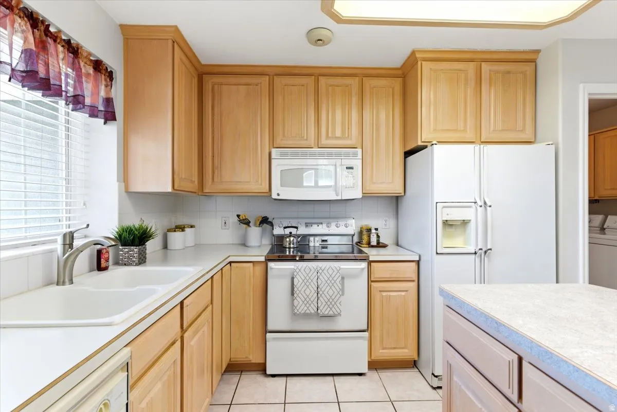 Kitchen featuring wood cabinetry, white appliances, tile flooring, white countertops, and a double basin sink