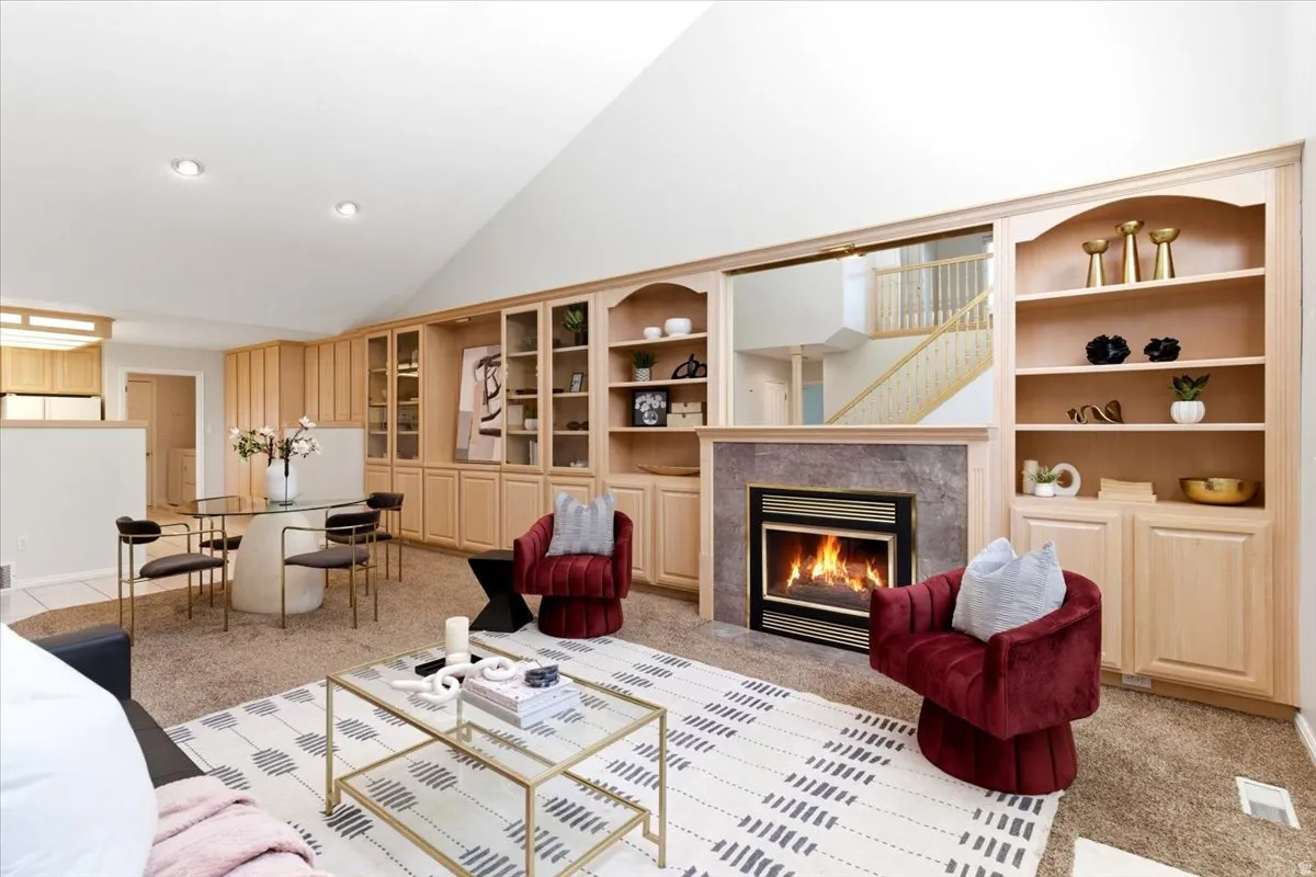 Living area featuring a fireplace with stone surround, built-in shelving, vaulted ceiling, and recessed lighting
