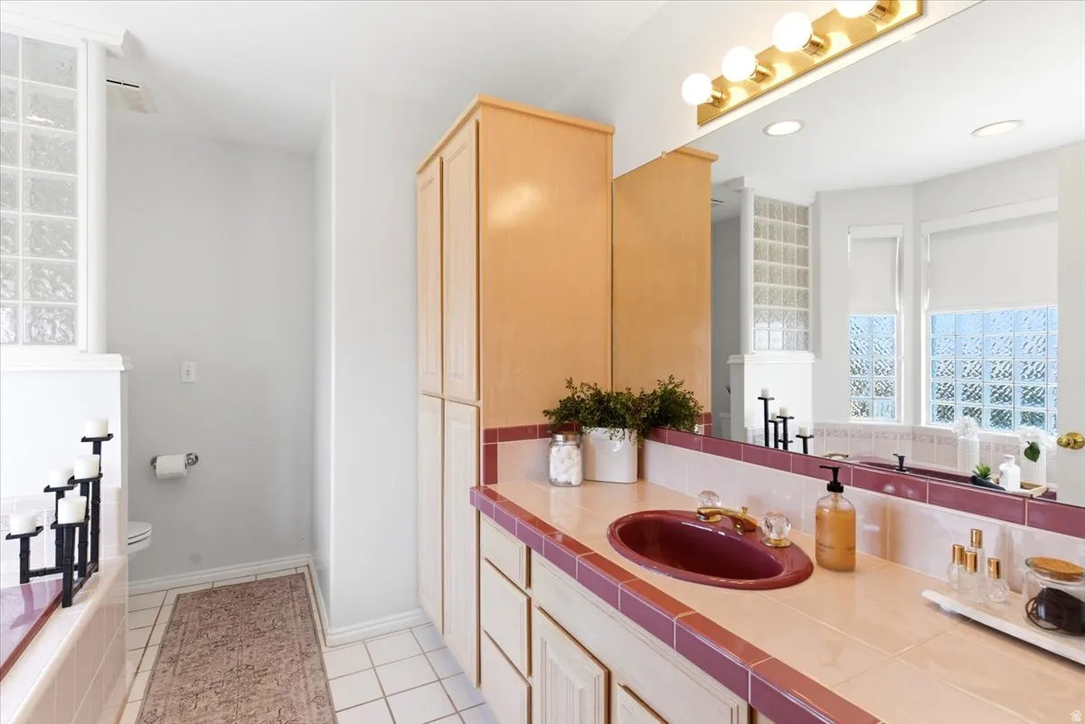 Primary bathroom with vanity, sink, tiled countertop, and wood-finish cabinetry