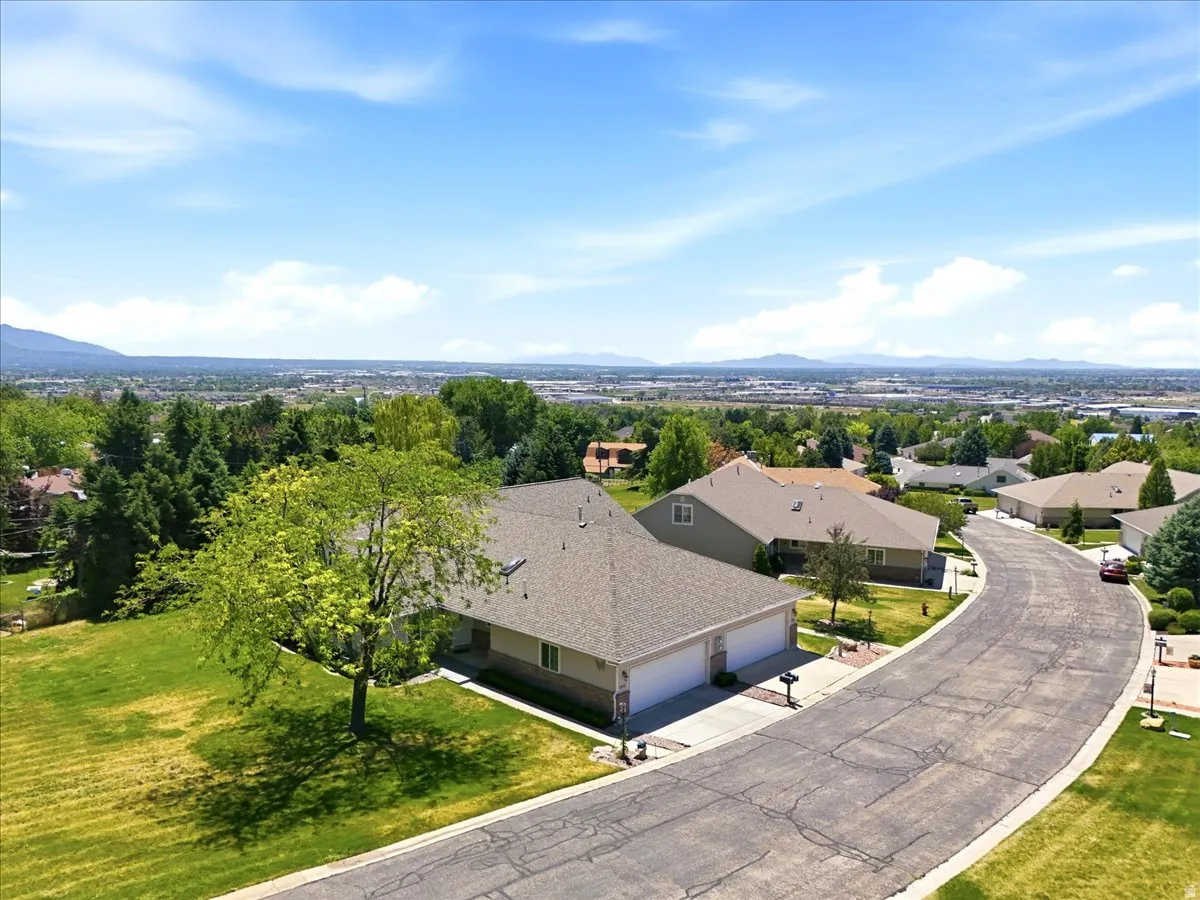 Residential property featuring a two-car garage, mature front yard tree, and an expansive lawn