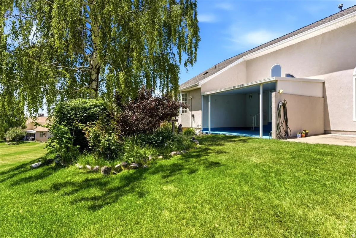 Expansive green lawn with mature landscaping and a covered patio featuring a blue-painted floor