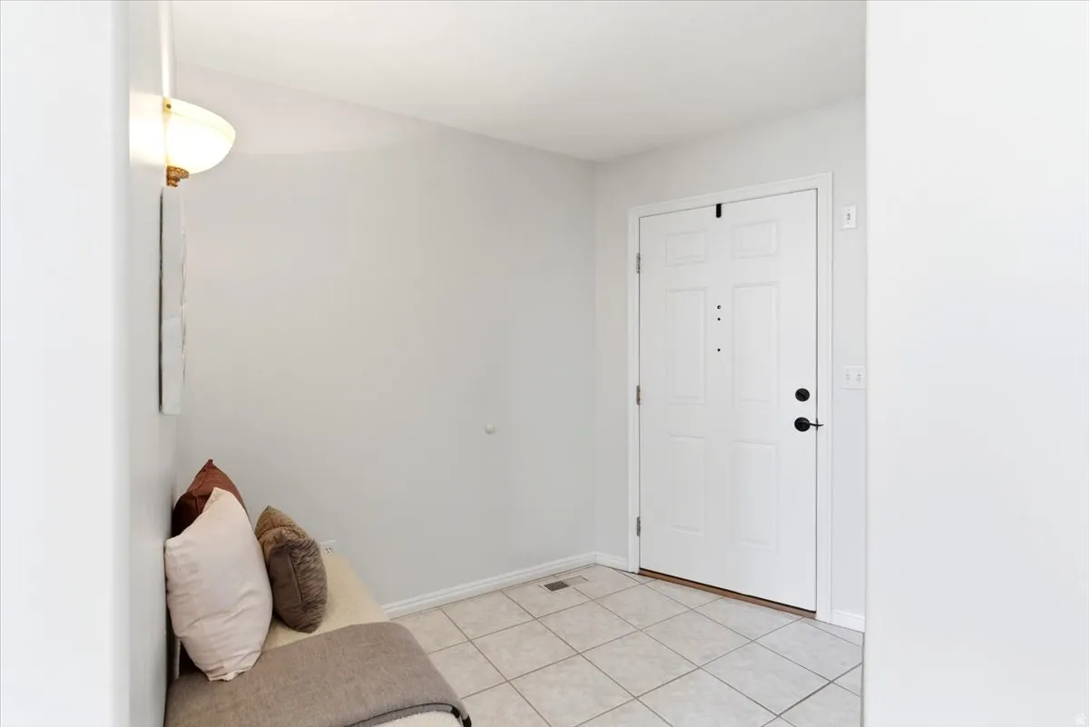 Entryway featuring a paneled door with matte black hardware, ceramic tile flooring, and a wall-mounted sconce