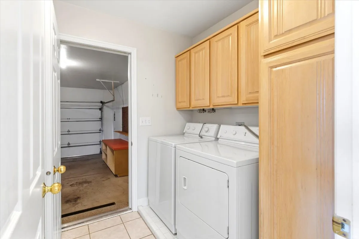 Laundry area with tile flooring and wood cabinetry, offering direct access to the garage with a built-in workbench