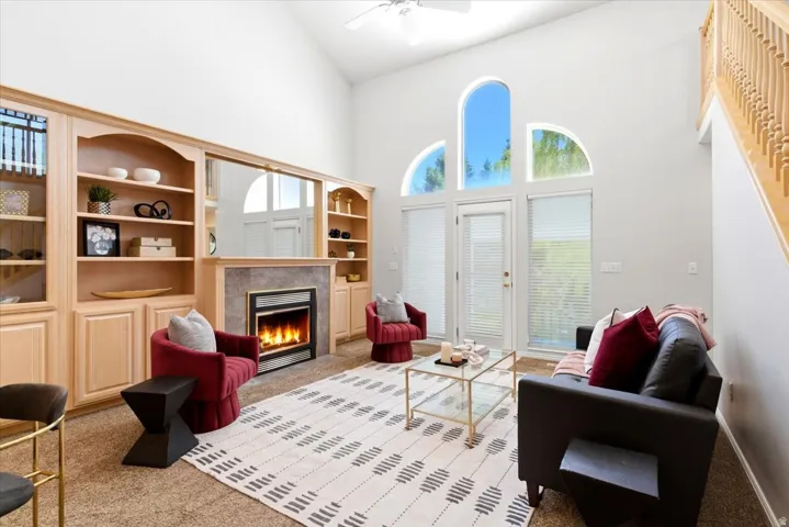 Living area featuring a vaulted ceiling with a ceiling fan, a built-in entertainment center with integrated shelving, and a fireplace with a stone surround