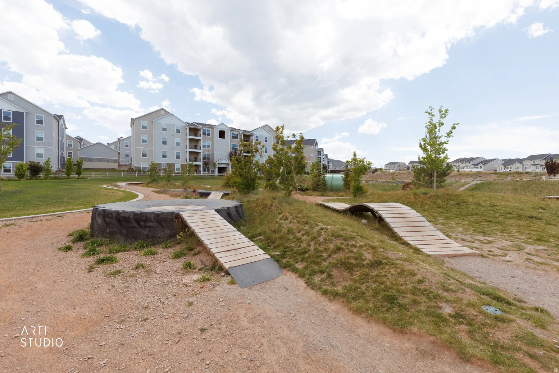 Outdoor recreational area featuring a dirt path, wooden ramps, and landscaped grassy mounds