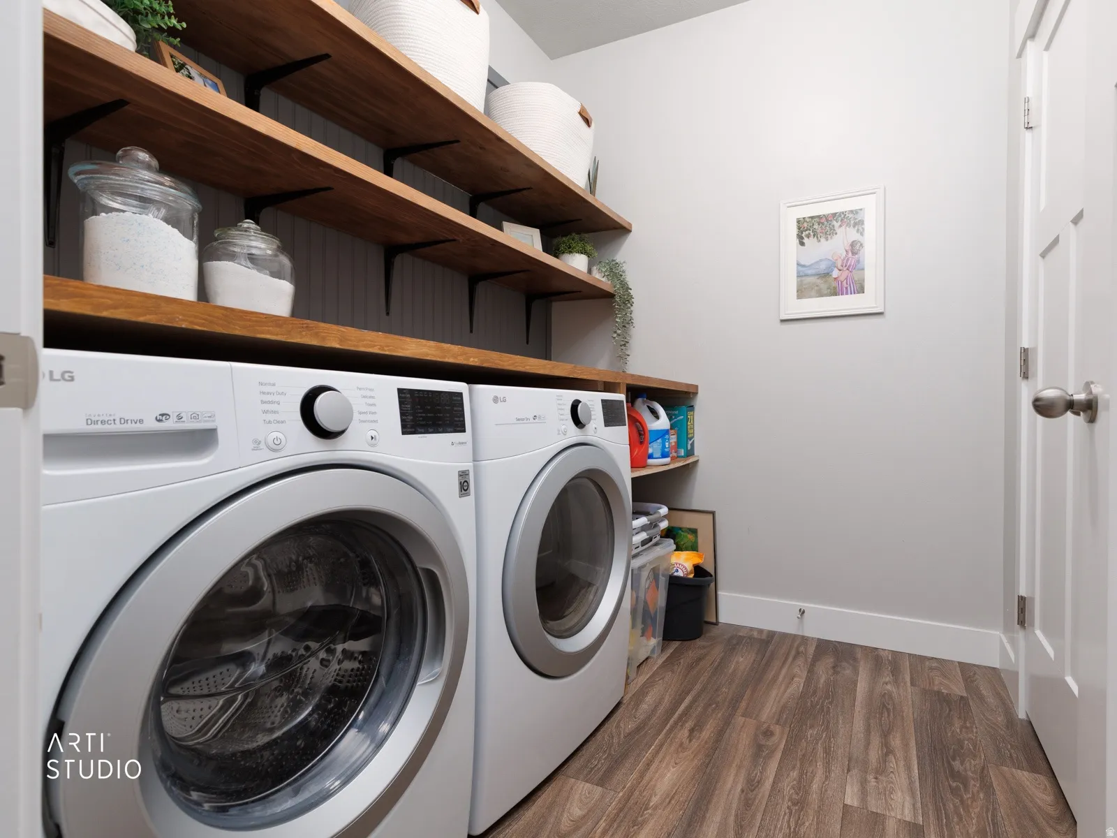 Dedicated laundry space featuring a wood-finish countertop, coordinating open shelving with black brackets, white beadboard paneling, and wood-finish flooring