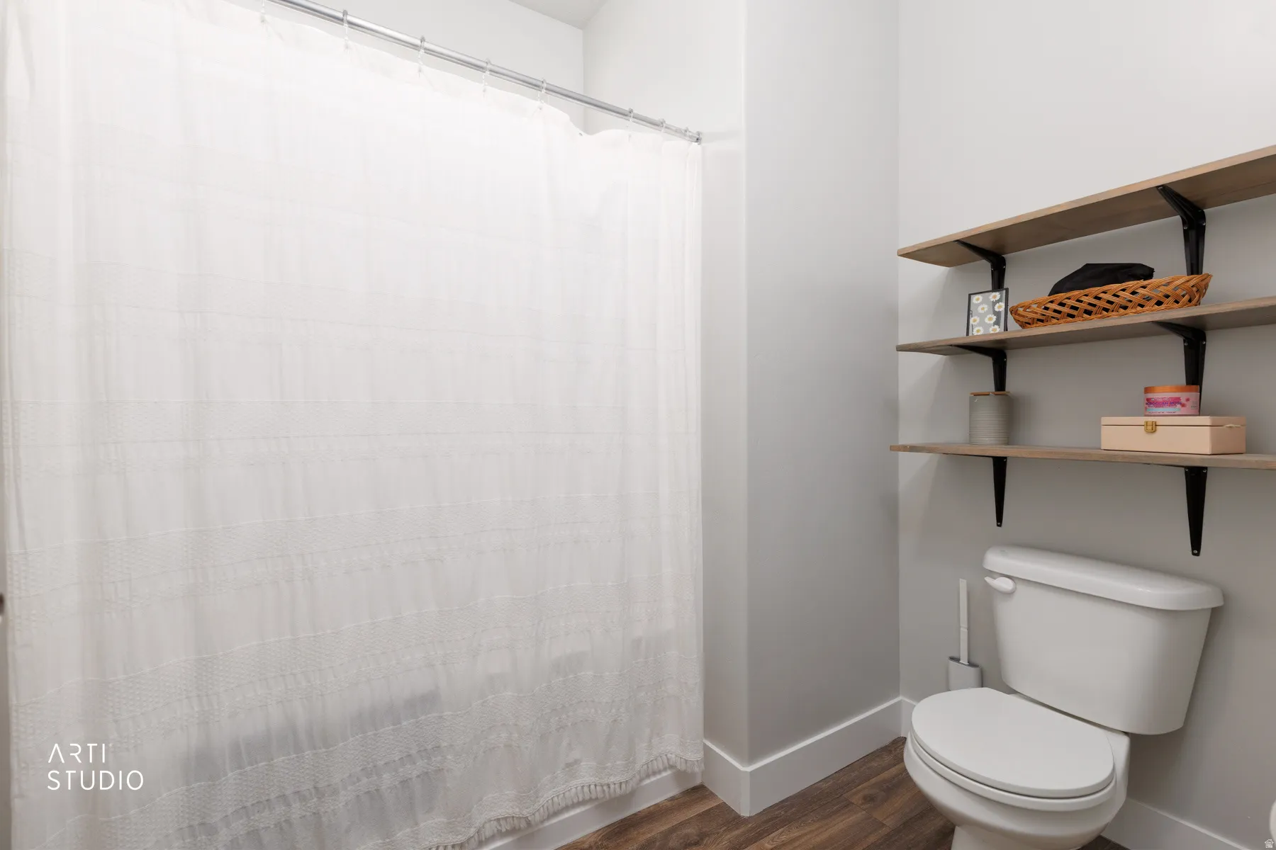Functional bathroom featuring wood-finish flooring, white baseboards, a standard toilet, and three wall-mounted shelving units with black brackets