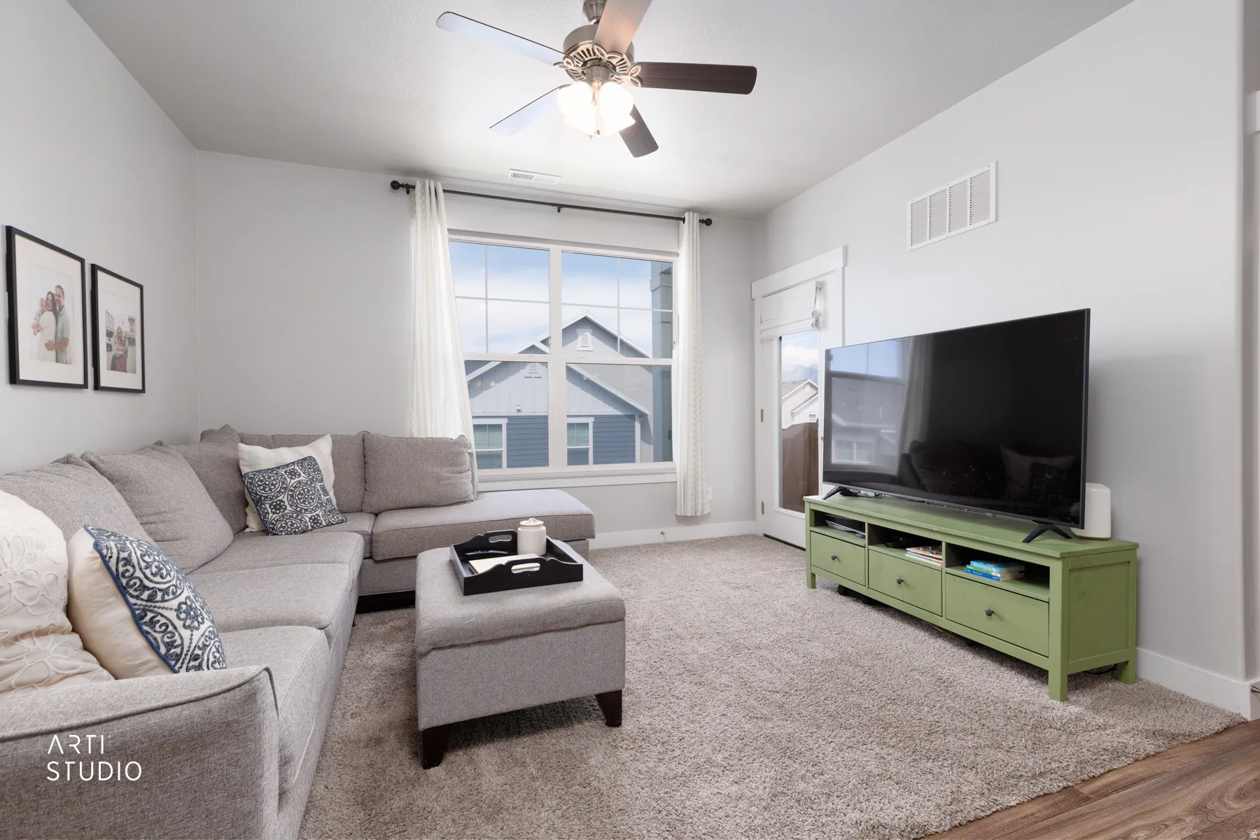 Open-concept living space featuring a ceiling fan with integrated lighting, a large window with white trim, and light gray walls