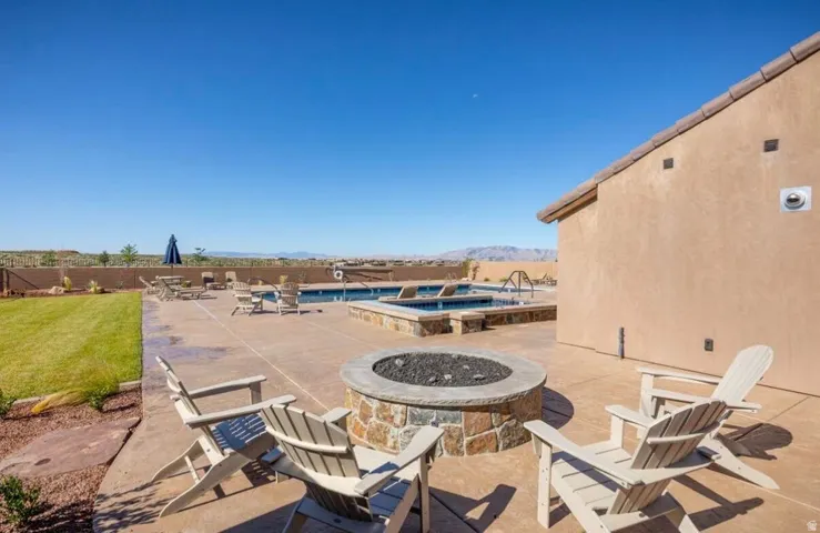 Expansive backyard patio featuring a stone fire pit with surrounding seating, a built-in swimming pool, and an integrated spa