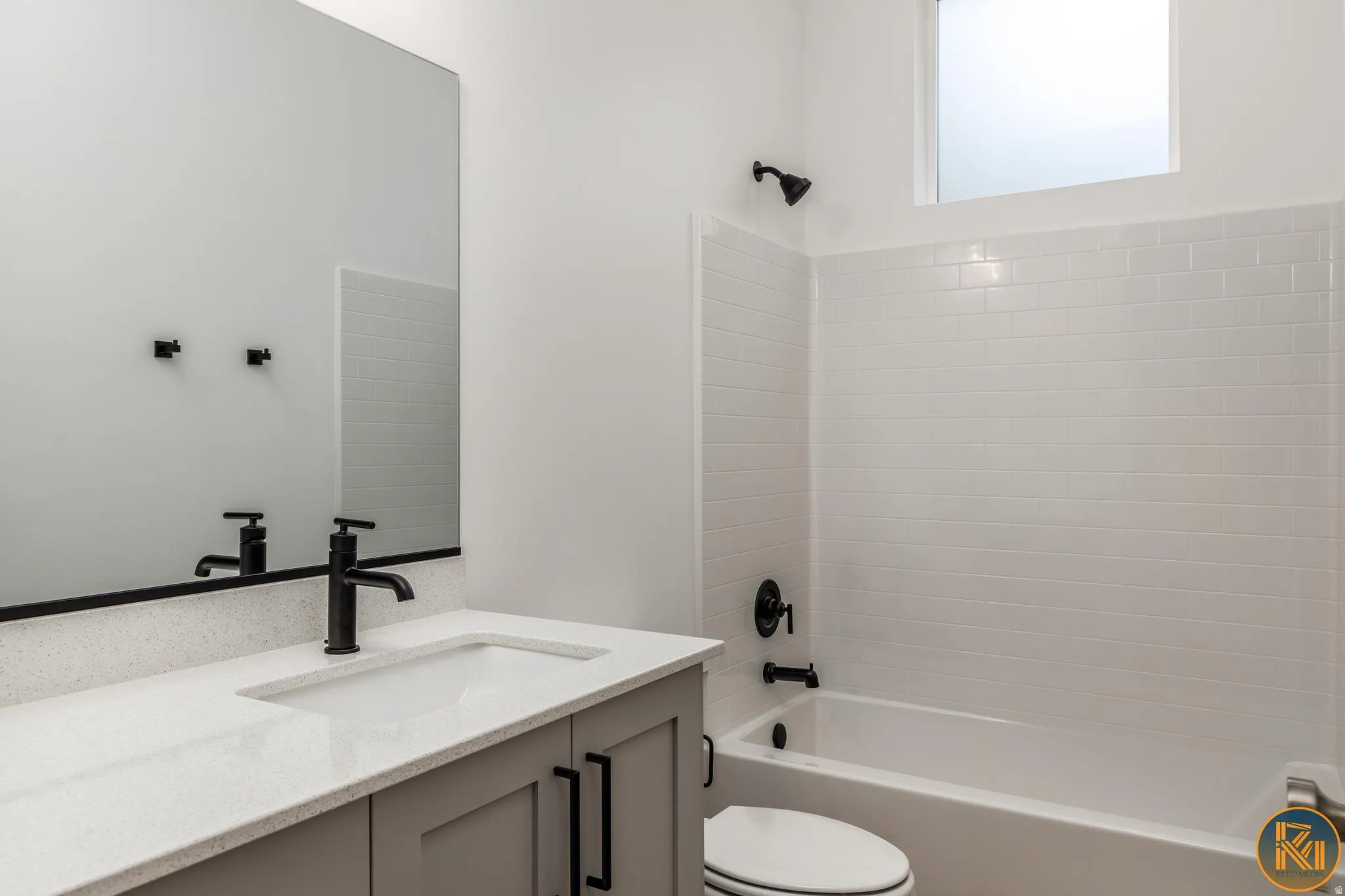 Bathroom featuring a bathtub and shower combination with white subway tile surround, white vanity with integrated sink and speckled countertop, matte black fixtures, and a rectangular mirror