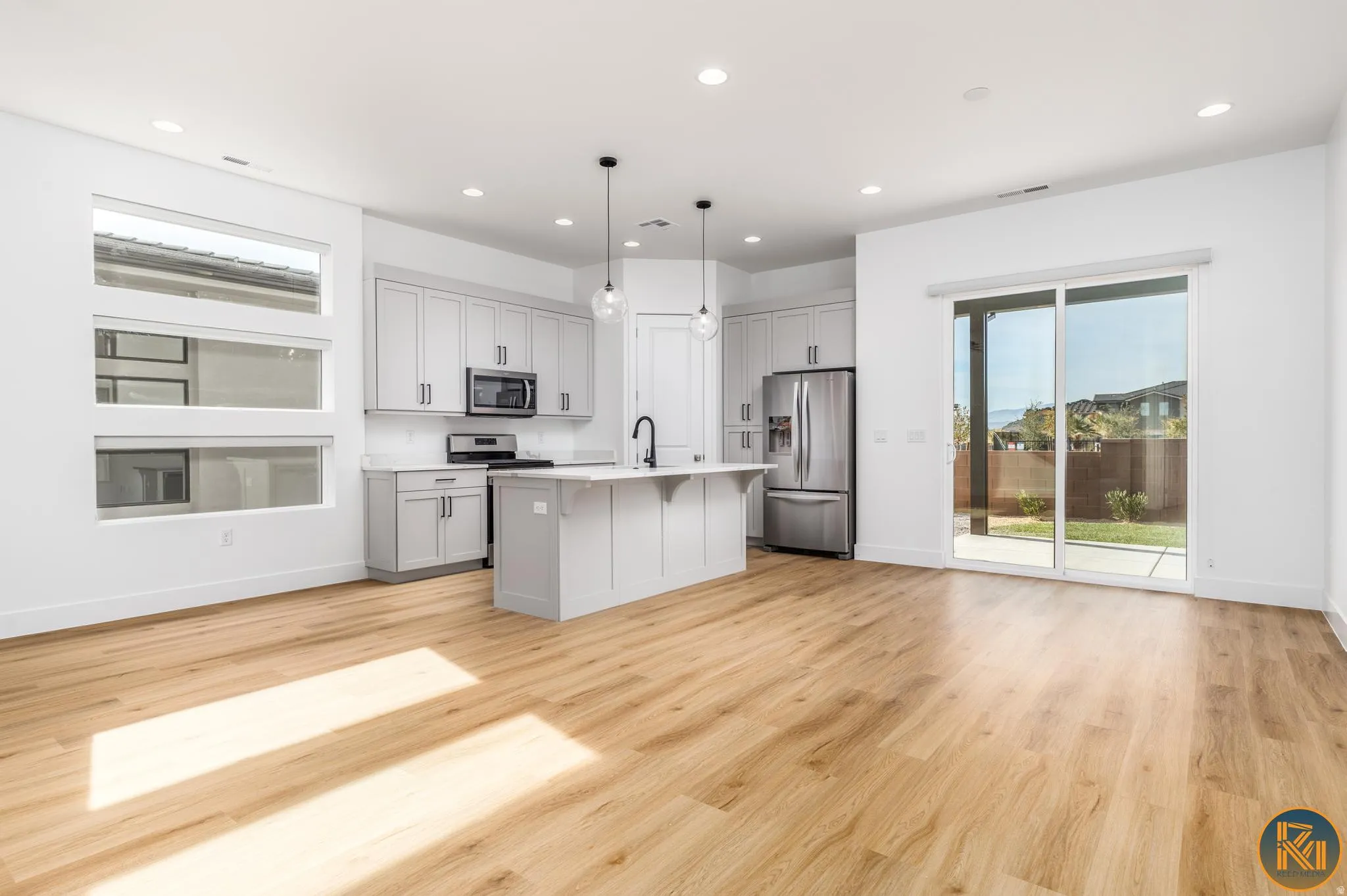 Open-concept living space featuring wood-finish flooring, a modern kitchen island with pendant lighting, stainless steel appliances, and sleek gray cabinetry