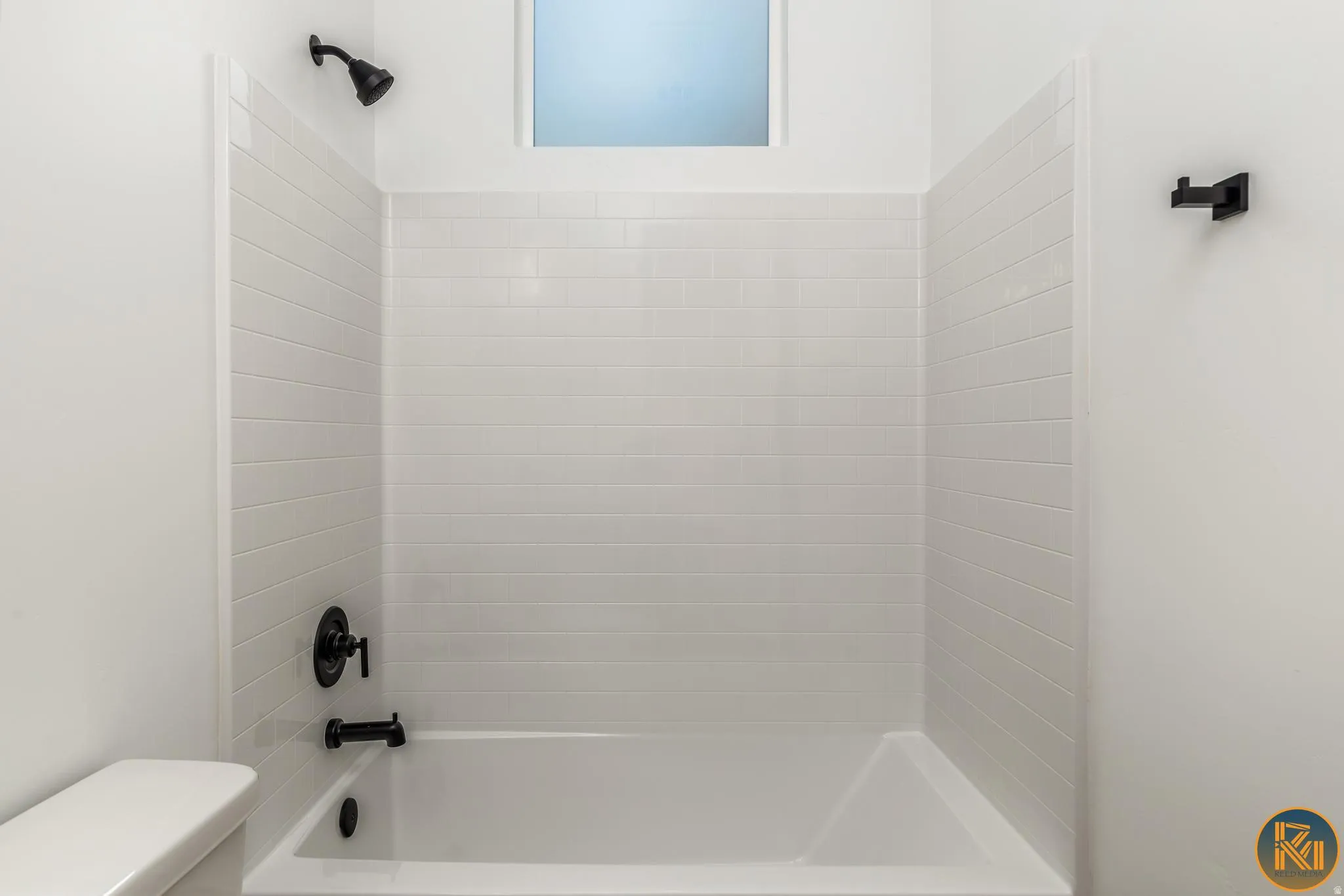 Bathtub with white subway tile surround, matte black shower fixtures, and frosted window