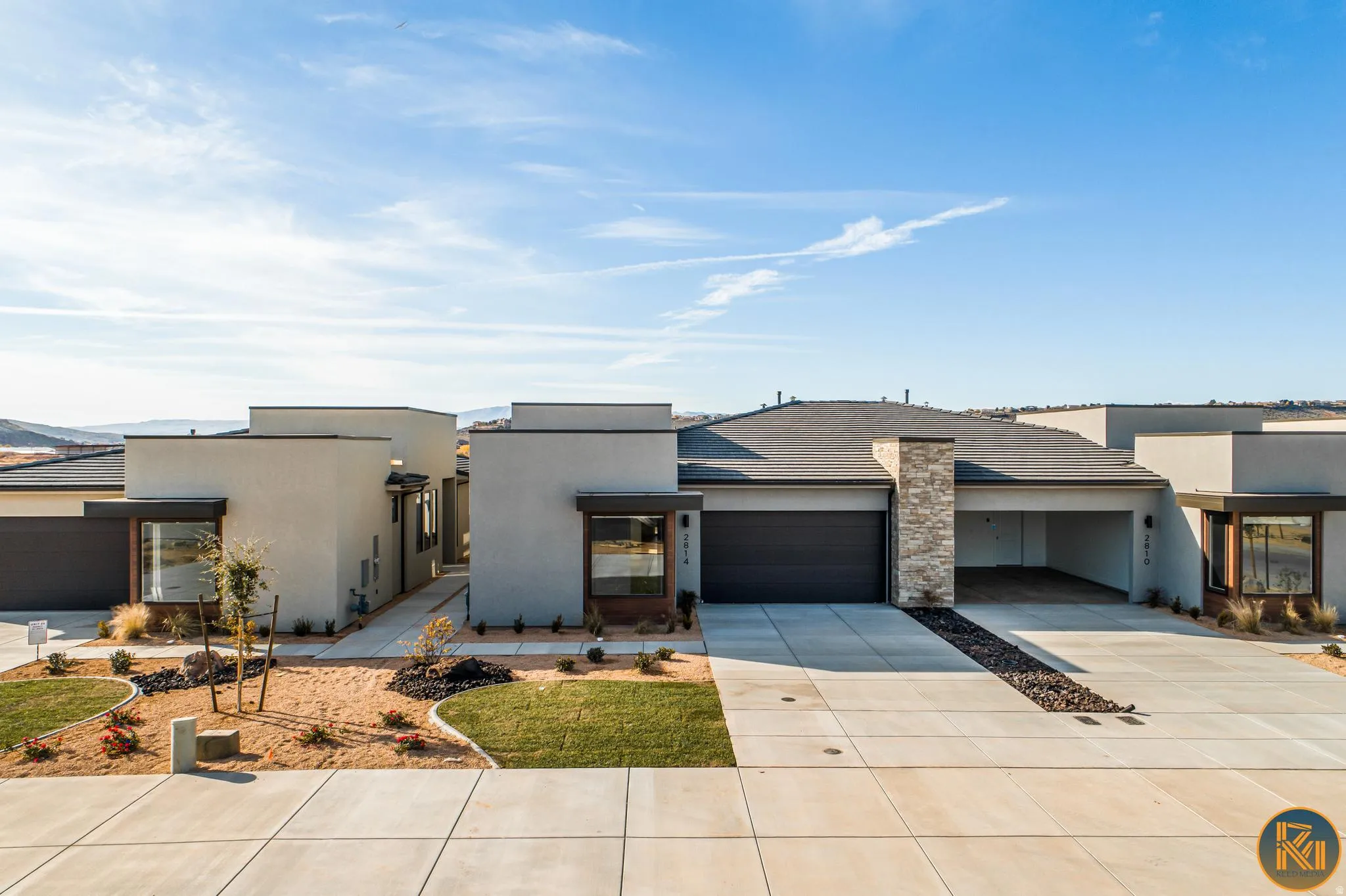 Modern stucco exterior with a dark gray garage door, stone pillar accent, and desert landscaping