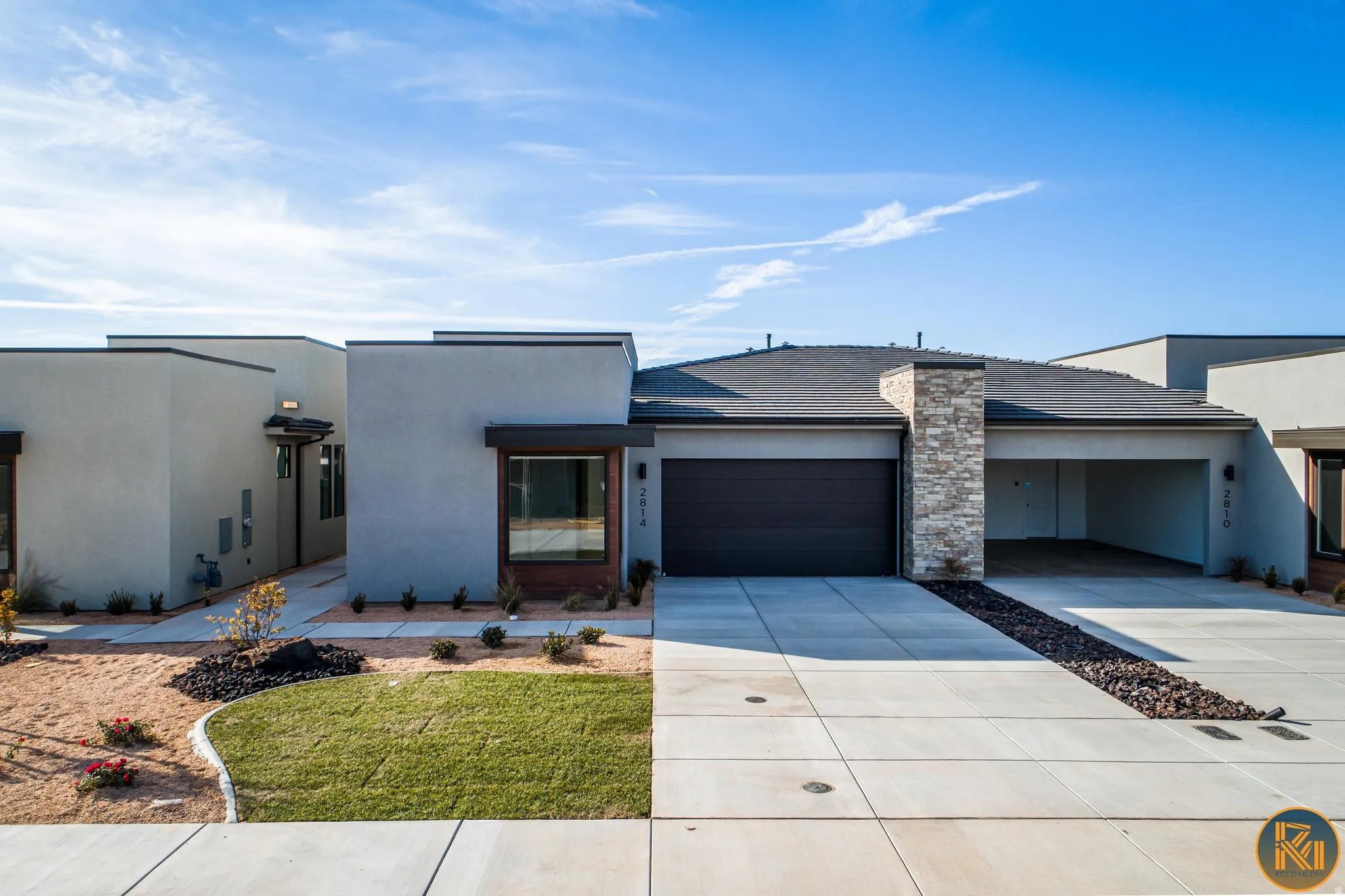 Modern architectural residence featuring a two-car garage, an additional carport, and a stone accent column