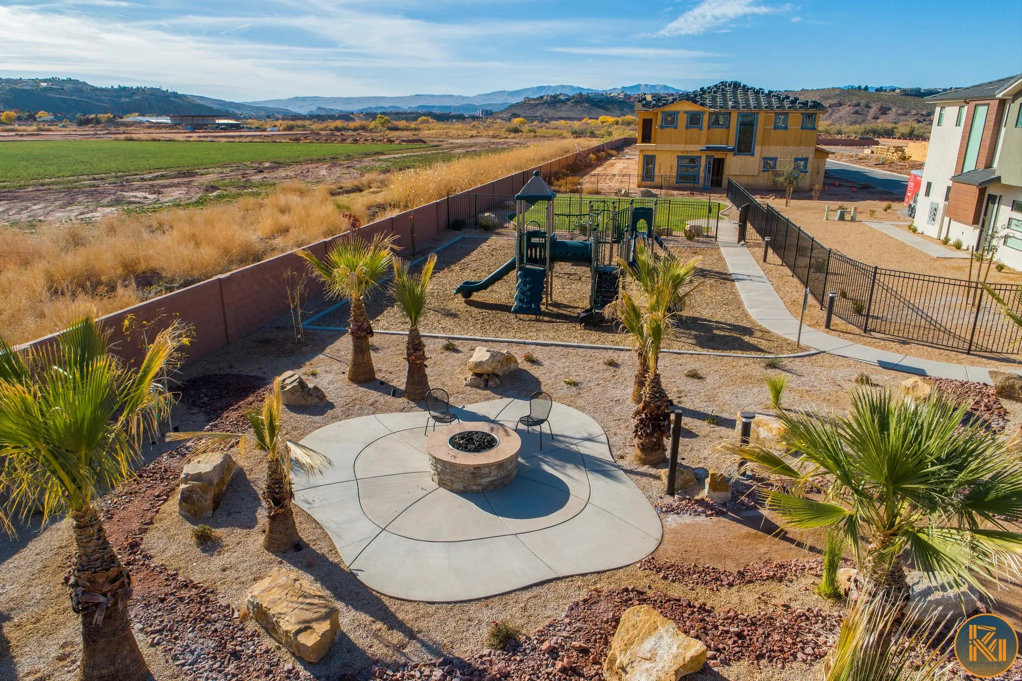 Expansive outdoor area featuring a built-in fire pit with an organic-shaped concrete patio, multiple mature palm trees, and decorative rock landscaping