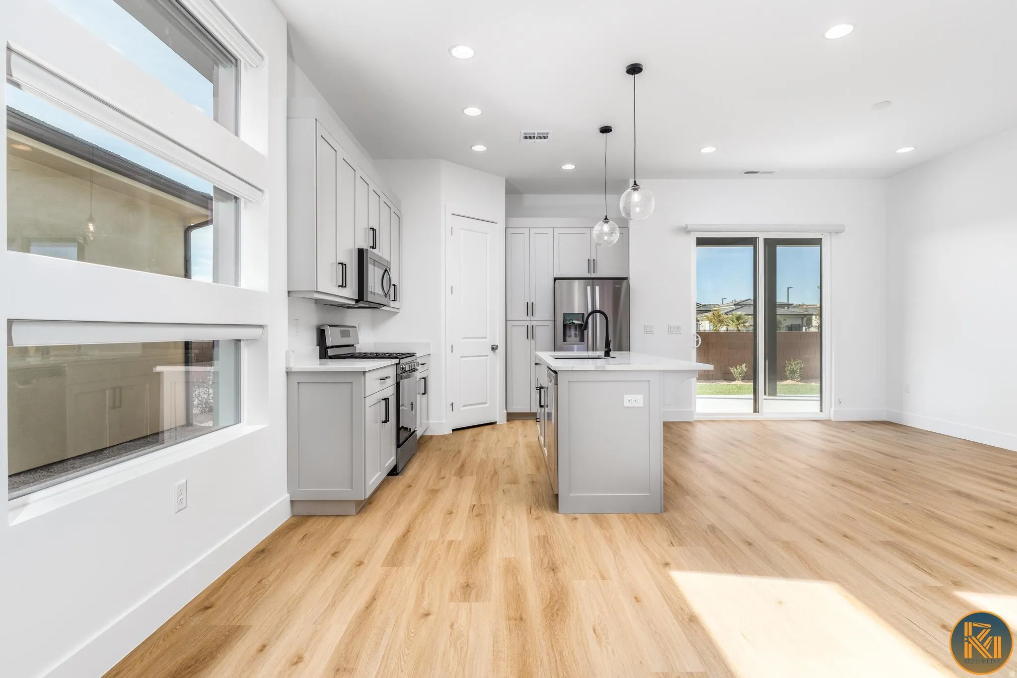 Open-concept living space featuring wood-finish flooring, a kitchen island with seating, a stainless steel refrigerator, and light gray cabinetry