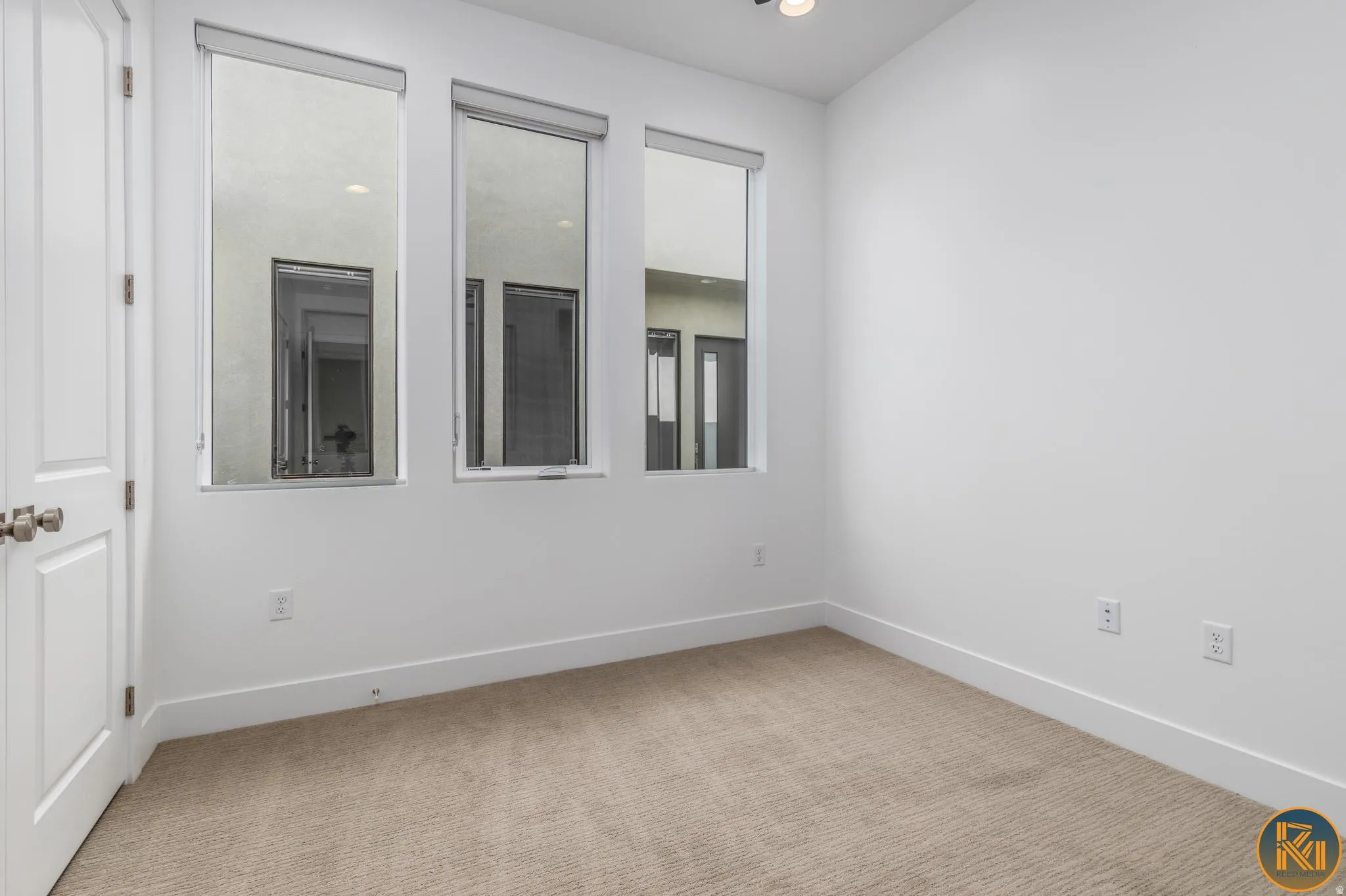 Room featuring three vertical windows, white walls, and neutral-toned carpet flooring