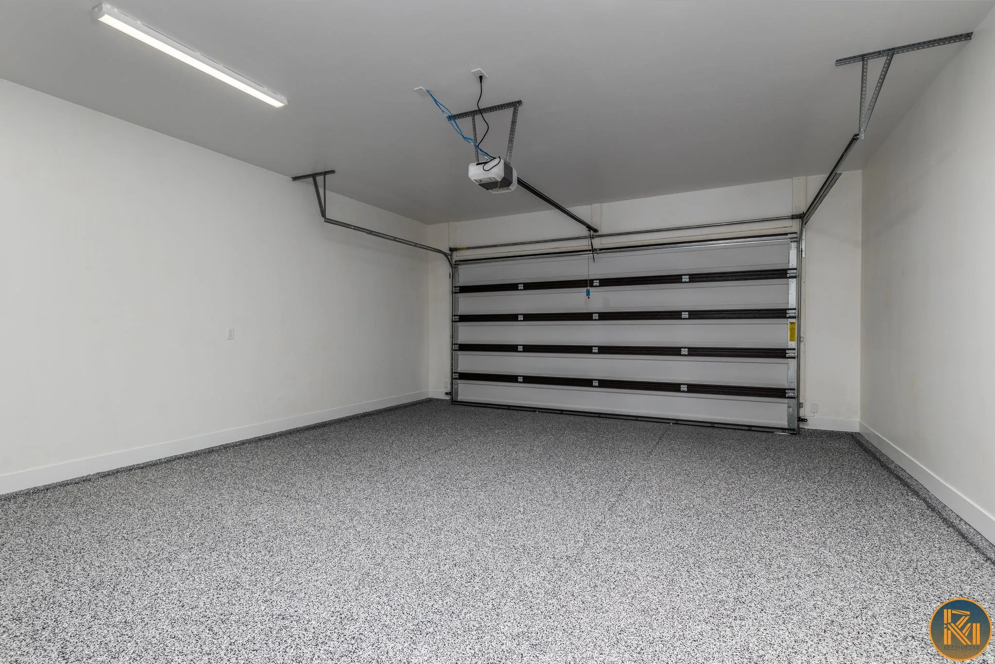 Spacious garage featuring a durable epoxy floor coating, white painted walls, a sectional garage door with automatic opener, and overhead fluorescent lighting