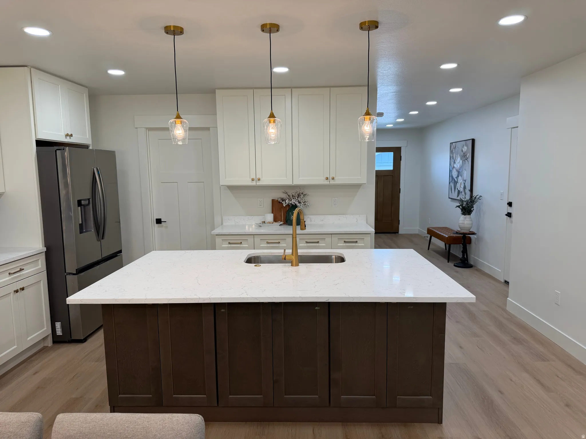 Kitchen island with a white countertop and dark wood-finish cabinetry, illuminated by three pendant lights