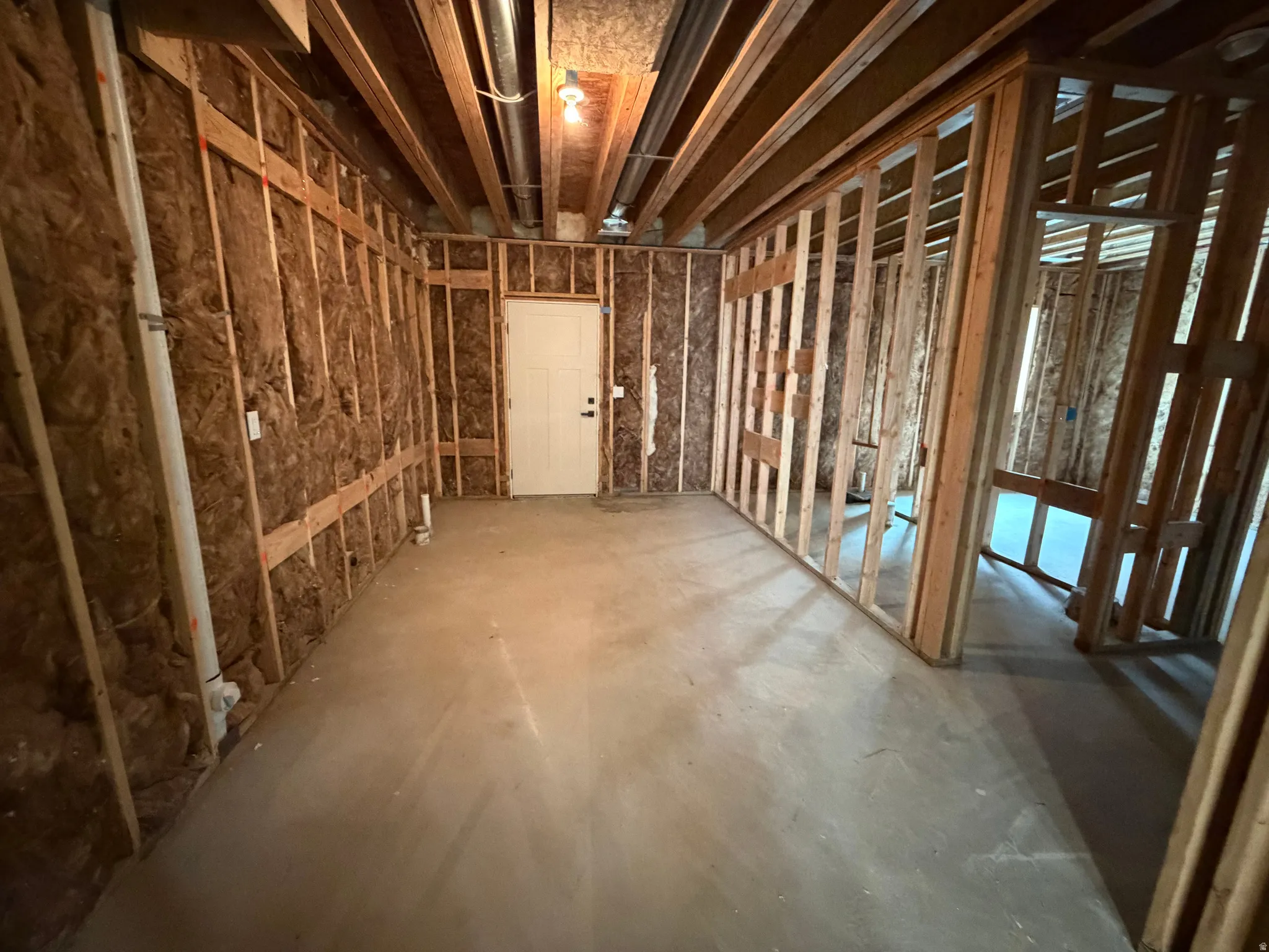 Unfinished basement space featuring exposed wood framing, concrete flooring, visible insulation, and a white interior door