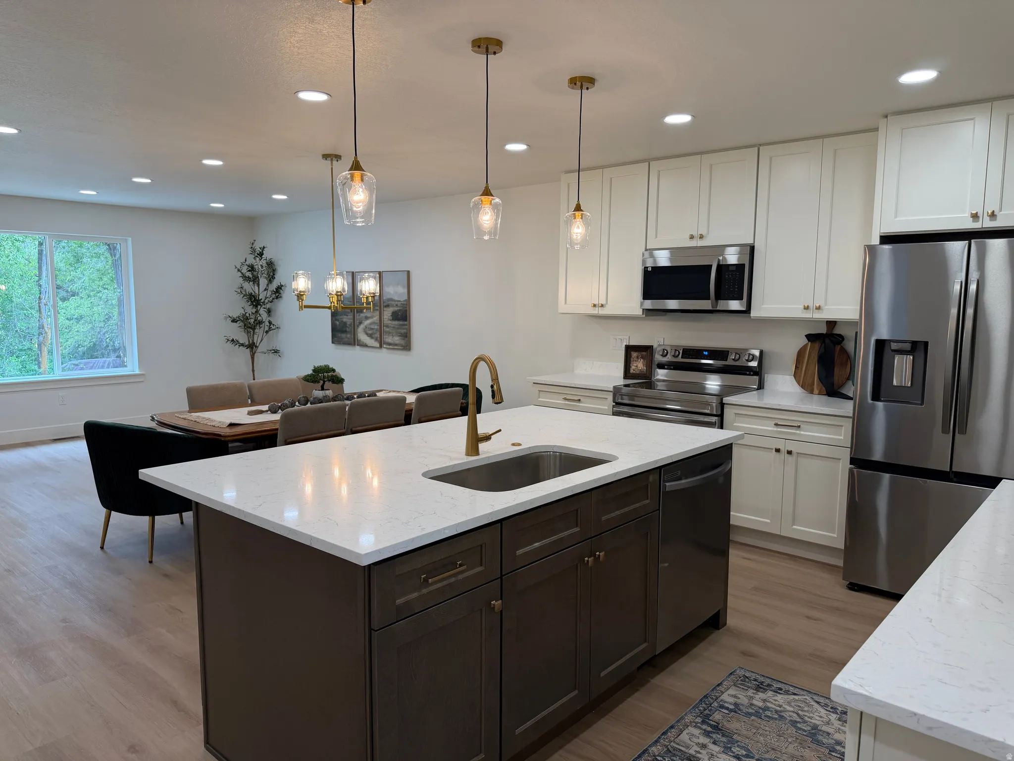 Open-concept kitchen featuring an oversized island with an undermount sink, brass faucet, and white countertops