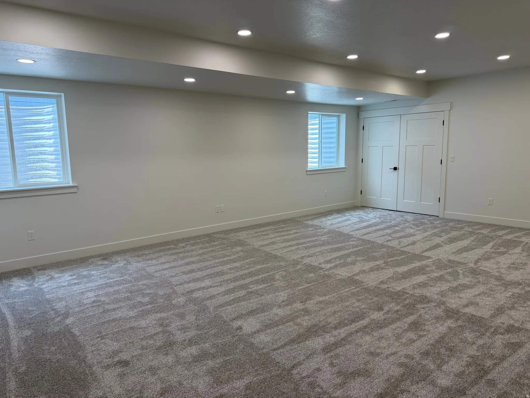 Spacious room featuring new patterned carpet, recessed lighting, two windows with blinds, and white double doors