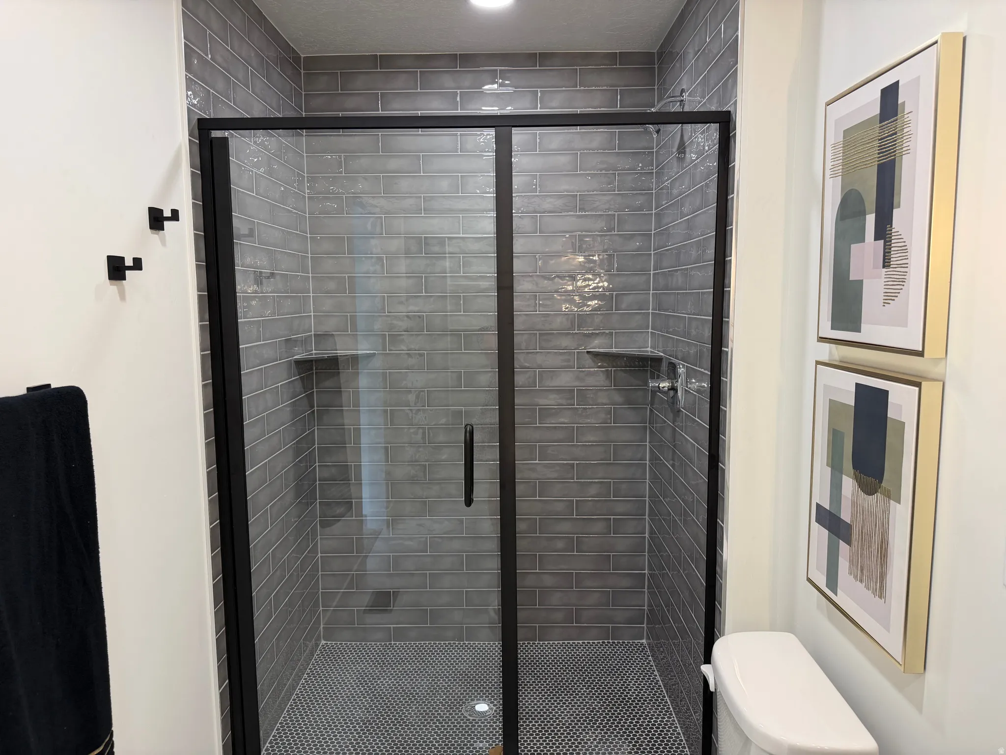 Shower enclosure featuring black-framed glass doors, grey subway tile surround, and built-in shelving