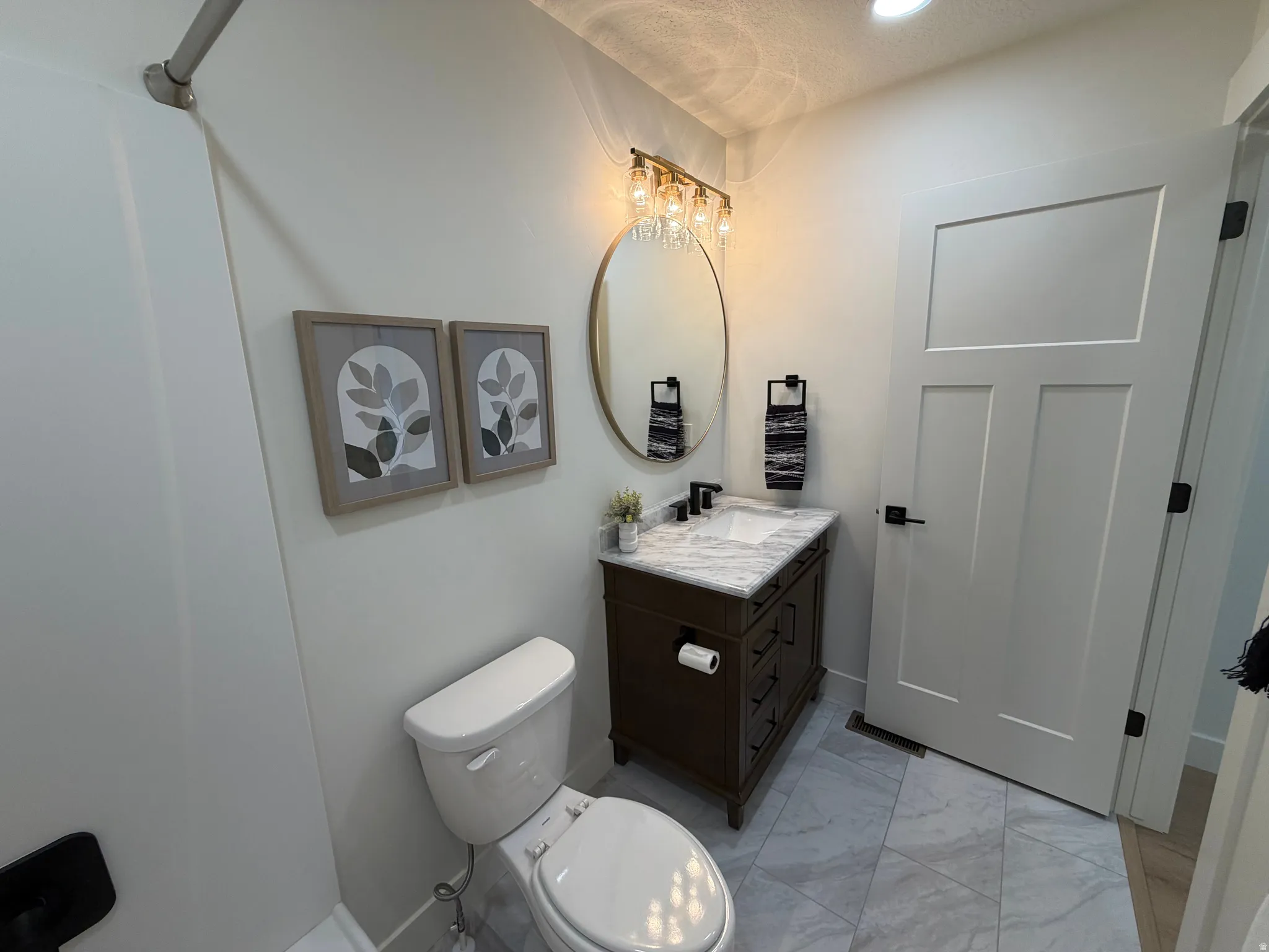 Bathroom featuring a dark wood vanity with a white marble countertop and integrated sink, matte black faucet, and oval gold-framed mirror