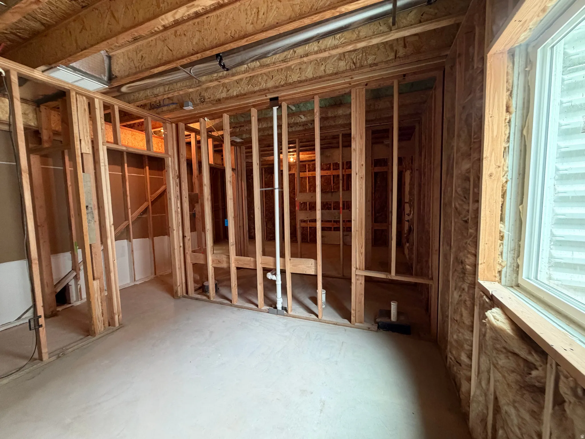 Unfinished interior space with exposed wood framing, concrete flooring, and a large window providing natural light