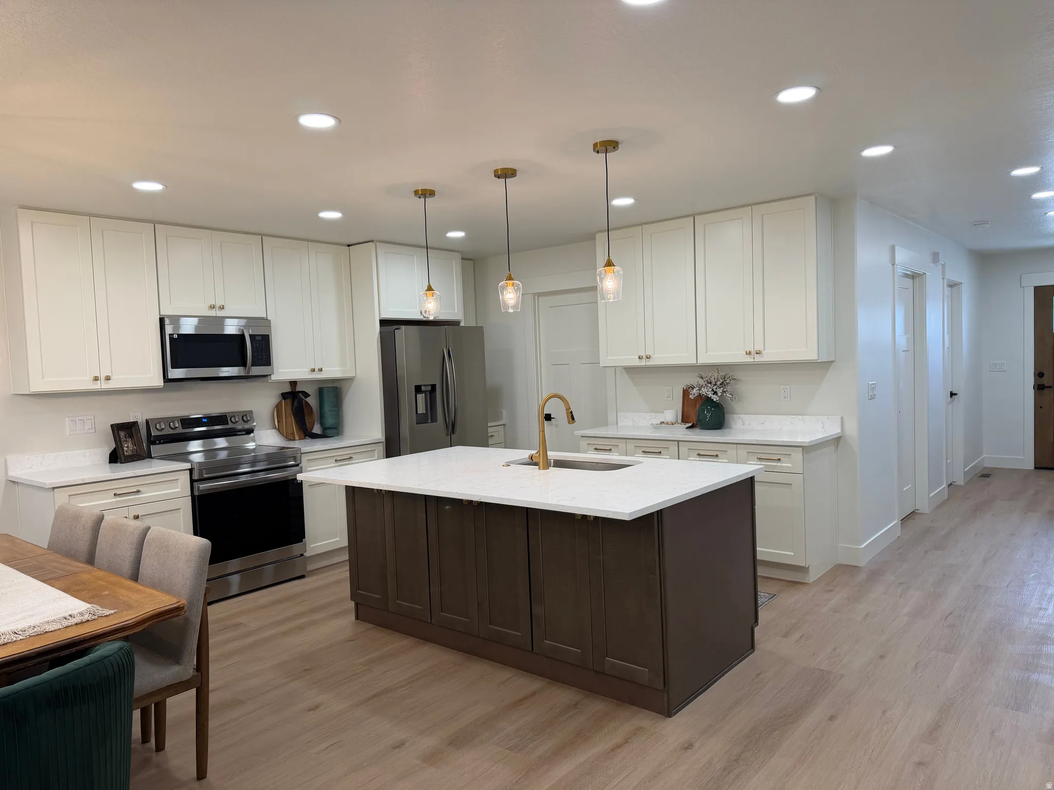 Contemporary kitchen featuring white cabinetry, stainless steel appliances, a center island with a white countertop and dark wood-finish base, and wood-finish flooring