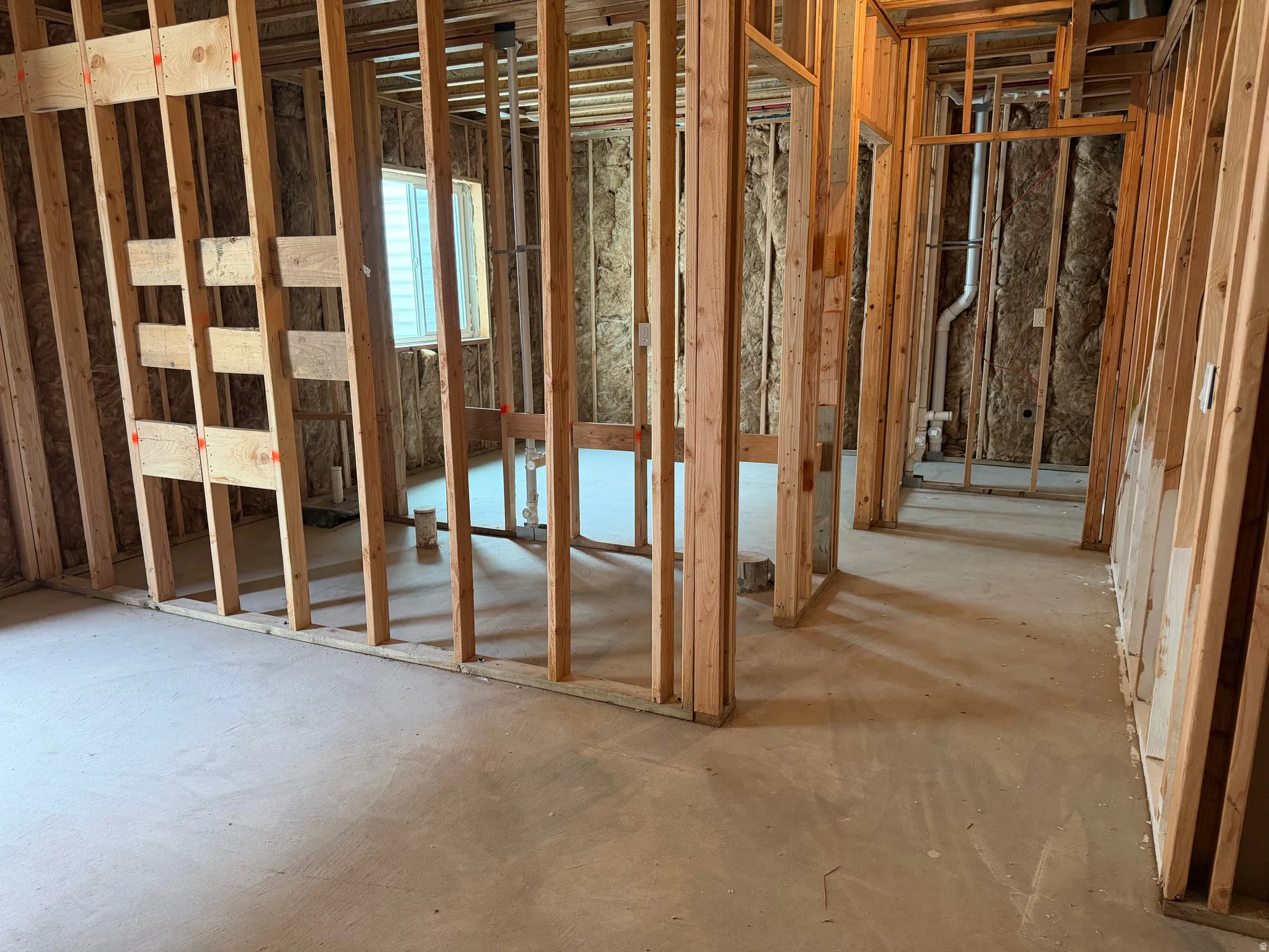 Unfinished interior space featuring wood framing, exposed insulation, a single window, and concrete flooring