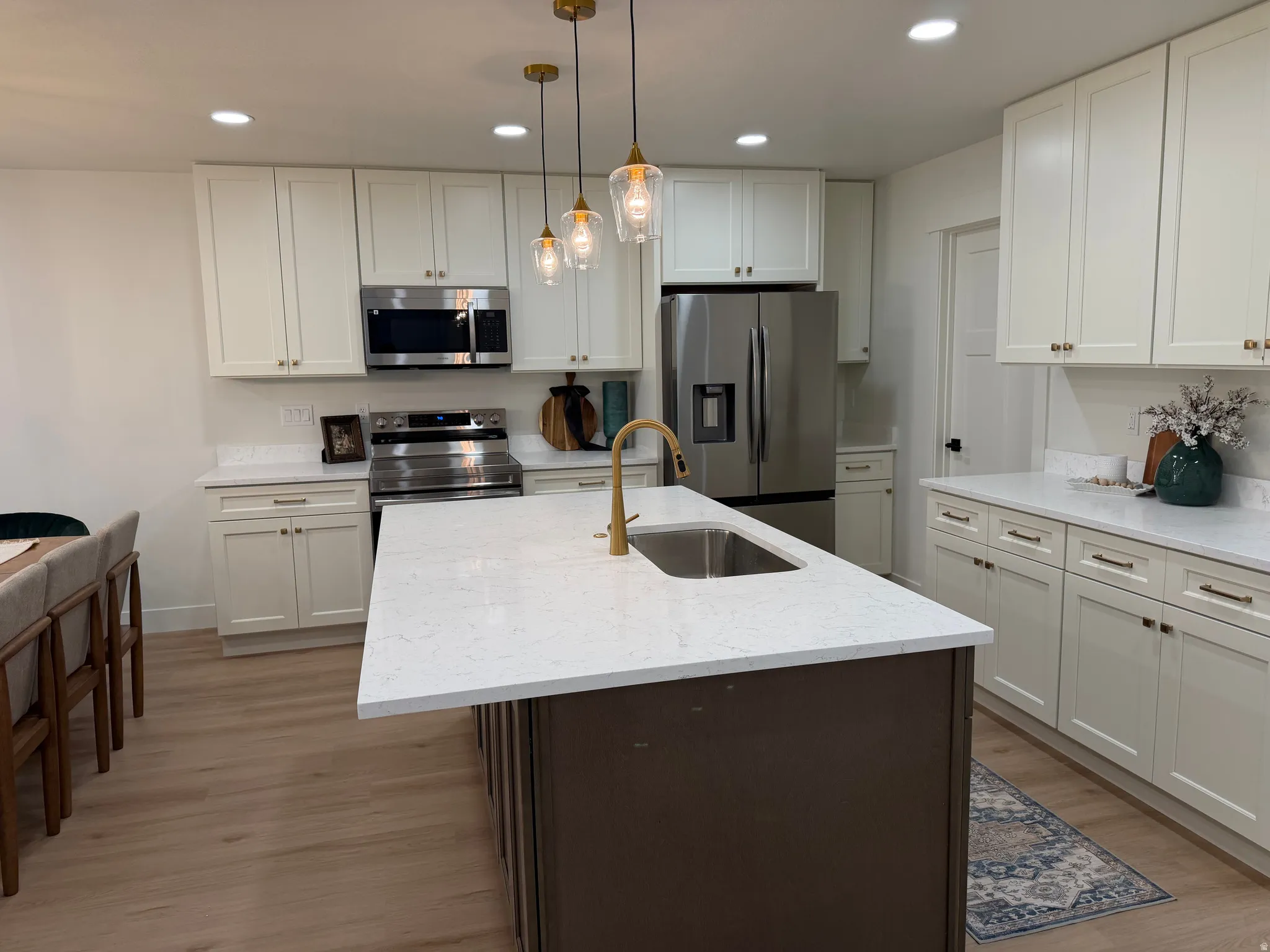 Kitchen featuring a central island with an undermount sink, brass faucet, and white countertop