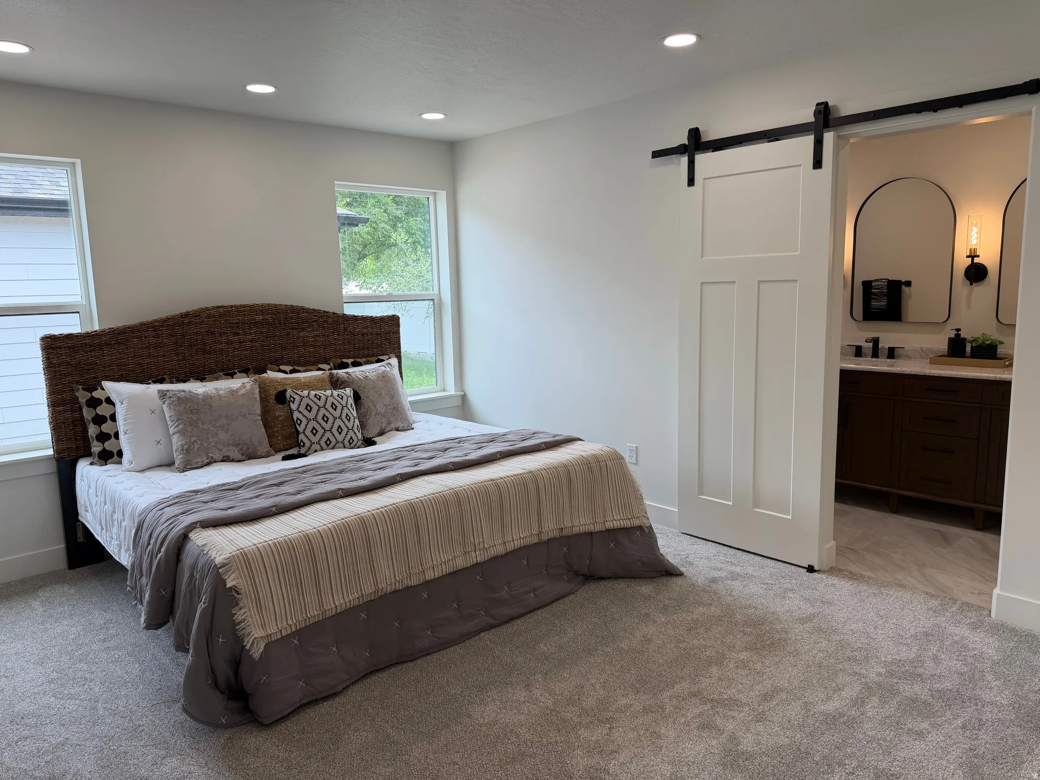 Spacious room featuring light gray carpeting, recessed ceiling lighting, and a barn door entry to a bathroom