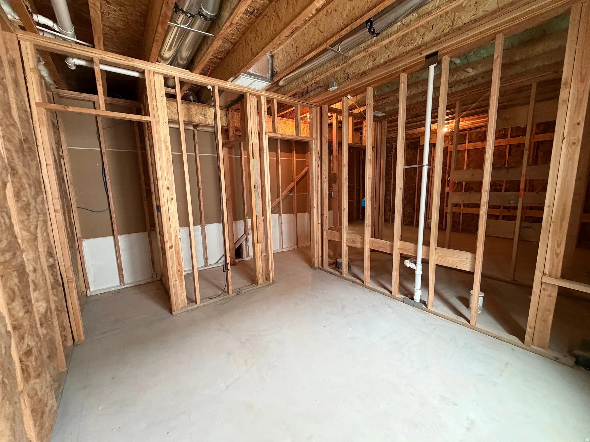 Unfinished basement featuring exposed wood framing, concrete flooring, visible overhead ductwork, and plumbing rough-ins