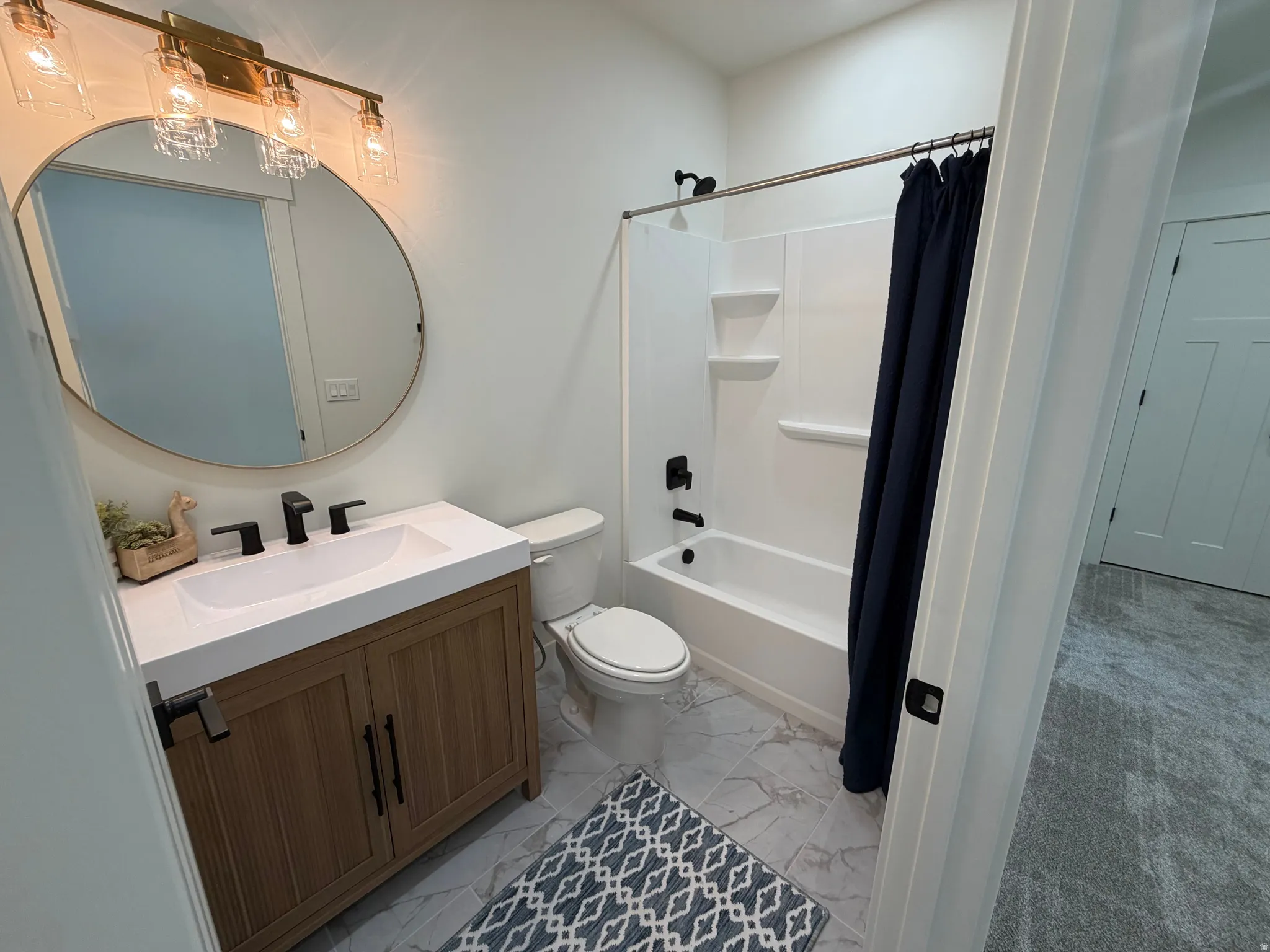 Bathroom featuring a wood-finish vanity with a white countertop and integrated sink, matte black faucet, and a round mirror