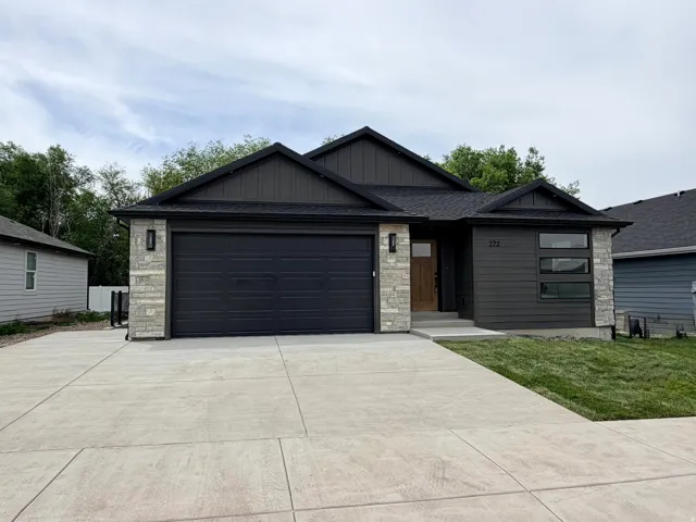 Modern single-story residence with a dark gray exterior, light-toned stone accents, and a contrasting wood-finish front door