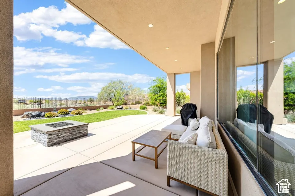 Expansive covered patio featuring a stone-clad fire pit, concrete flooring, and a manicured lawn