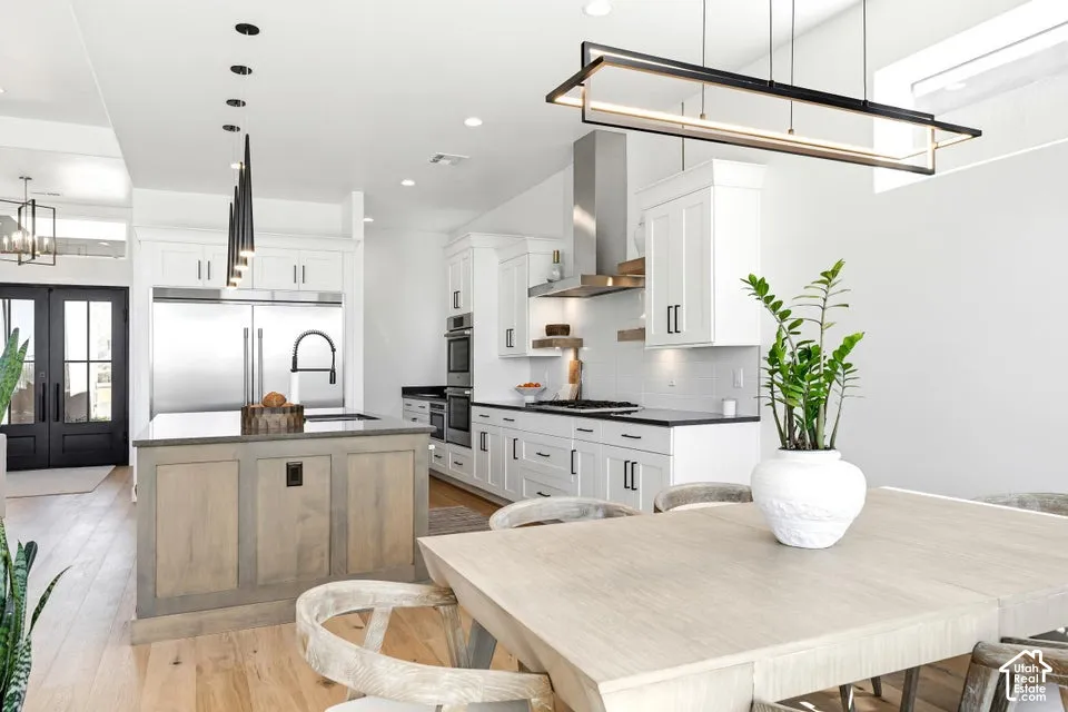 Open-concept kitchen featuring an oversized island with a dark countertop, white shaker cabinetry, stainless steel appliances, and wood-finish flooring