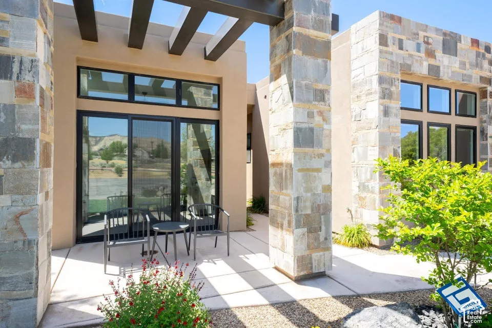 Exterior patio featuring a pergola, stone columns, stucco finish, and sliding glass doors with transom windows