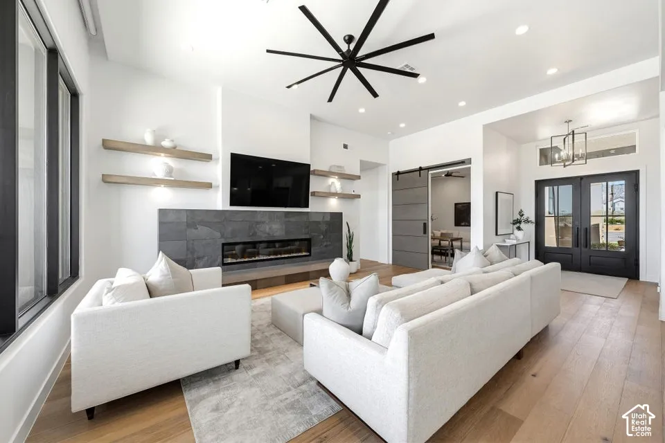 Spacious living area featuring light wood-finish flooring, a linear fireplace with a dark stone-clad surround, and a modern black ceiling fan