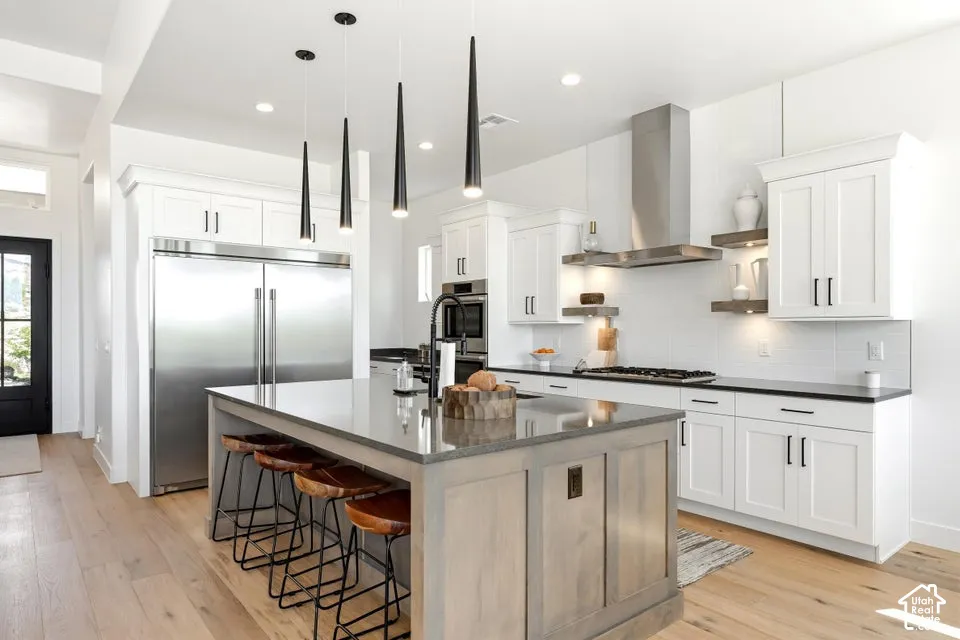 Contemporary kitchen featuring an expansive center island with seating, white shaker cabinetry, stainless steel appliances, a tile backsplash, and wood-finish flooring