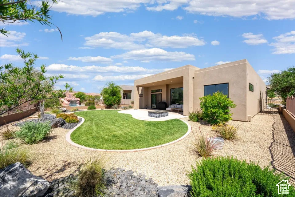 Contemporary stucco exterior with a covered patio, a manicured lawn, and a built-in fire pit
