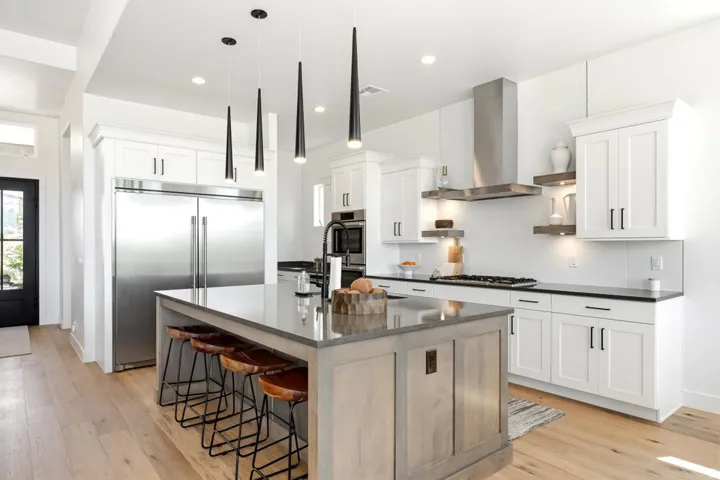 Contemporary kitchen featuring an expansive center island with seating, white shaker cabinetry, stainless steel appliances, a tile backsplash, and wood-finish flooring