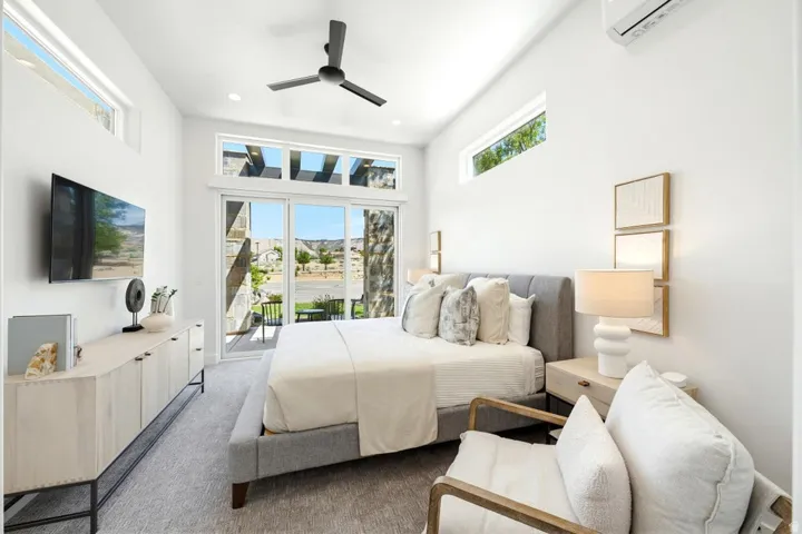 Light-filled bedroom featuring a vaulted ceiling with a modern ceiling fan, clerestory windows, and sliding glass doors opening to an outdoor patio