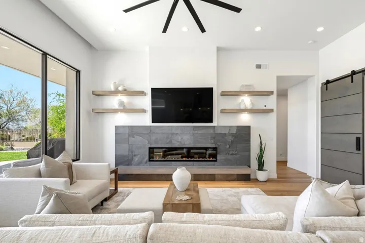 Spacious living area featuring a linear fireplace with a stone surround, wood-finish flooring, a contemporary ceiling fan, recessed lighting, and a barn door