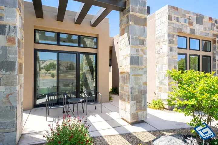 Exterior patio featuring a pergola, stone columns, stucco finish, and sliding glass doors with transom windows