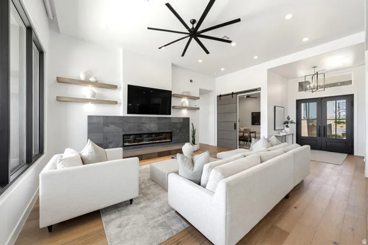 Spacious living area featuring light wood-finish flooring, a linear fireplace with a dark stone-clad surround, and a modern black ceiling fan