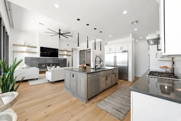 Open-concept living space featuring wood-finish flooring, a contemporary fireplace with dark stone surround, and recessed lighting