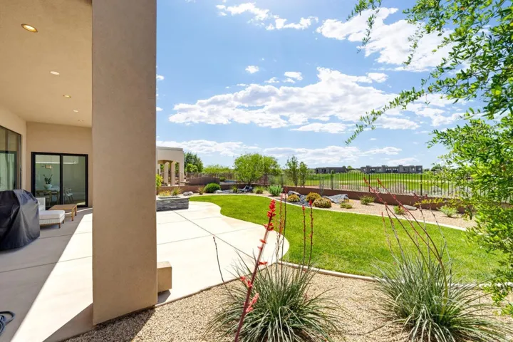 Expansive rear yard featuring a manicured lawn, concrete patio, and desert landscaping